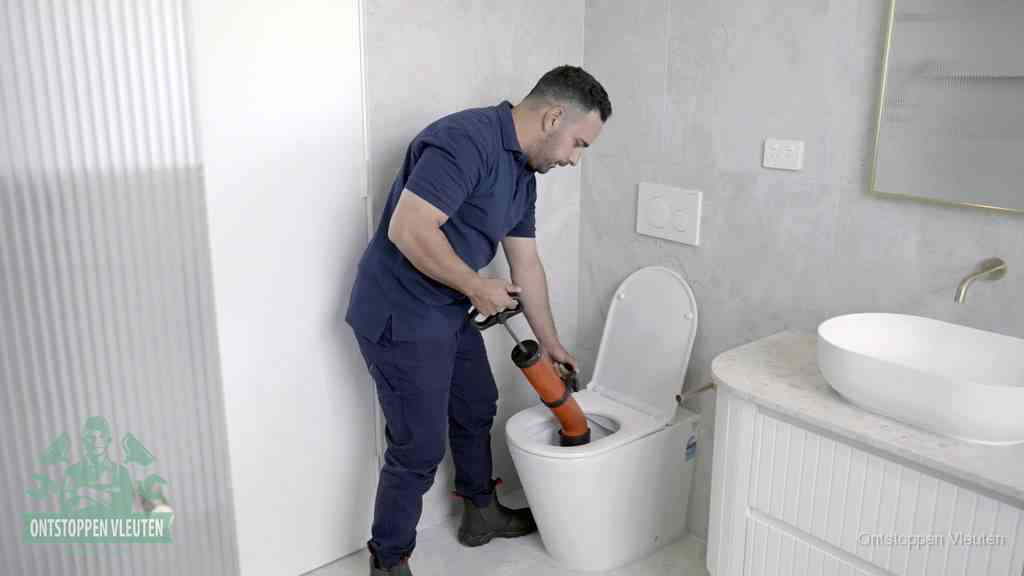 Een monteur buigt over een wandcloset en duwt met de hand een persluchtontstopper in de toiletpot om de verstopping handmatig los te maken in Vleuten