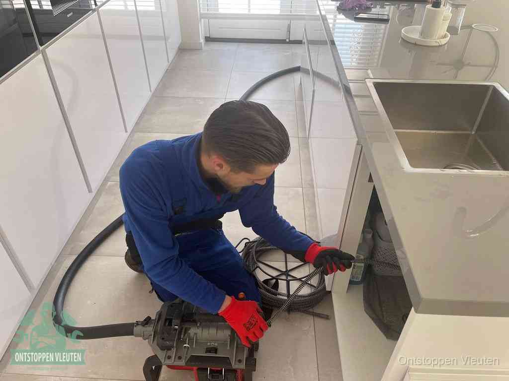 Een monteur ontstopt de keukenafvoer onder de spoelbak met een elektrische veermachine in Vleuten