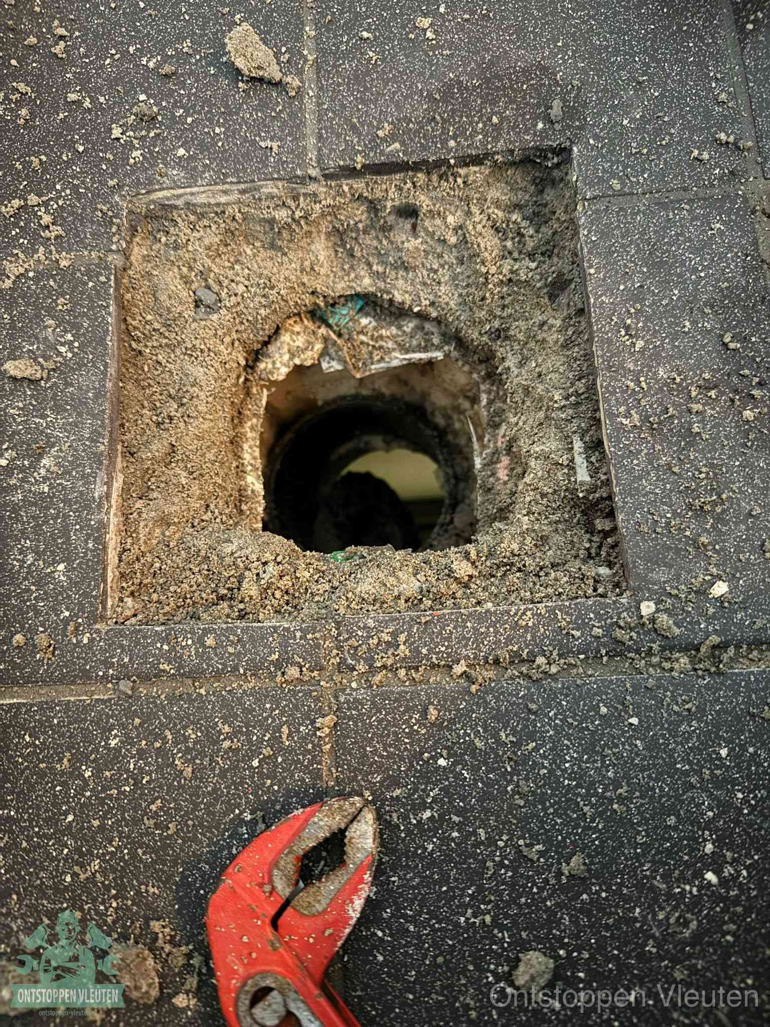 Een geopend rioolputje in een betontegelvloer met losgemaakt rooster en een zichtbare ronde afvoerbuis, het achterhalen waar de afvoerverstopping zit in Vleuten