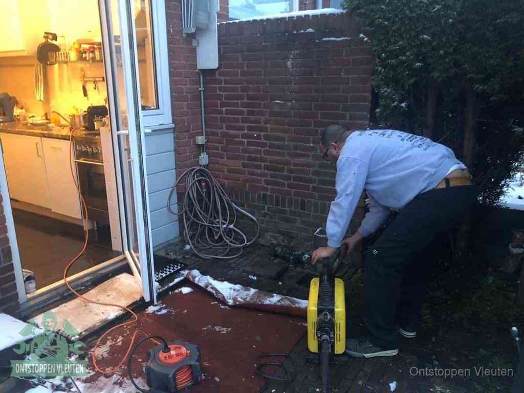 Een monteur werkt buiten bij een open riool-/grondput met een elektrische ontstoppingsmachine om een verborgen afvoerprobleem op te sporen in Vleuten