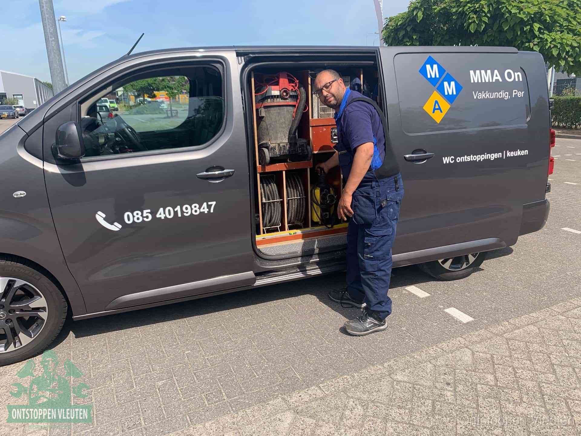 Een monteur bij de open schuifdeur van zijn bedrijfsbus op een parkeerplaats, klaar om de oorzaak van terugkerende afvoerverstoppingen aan te pakken in Vleuten