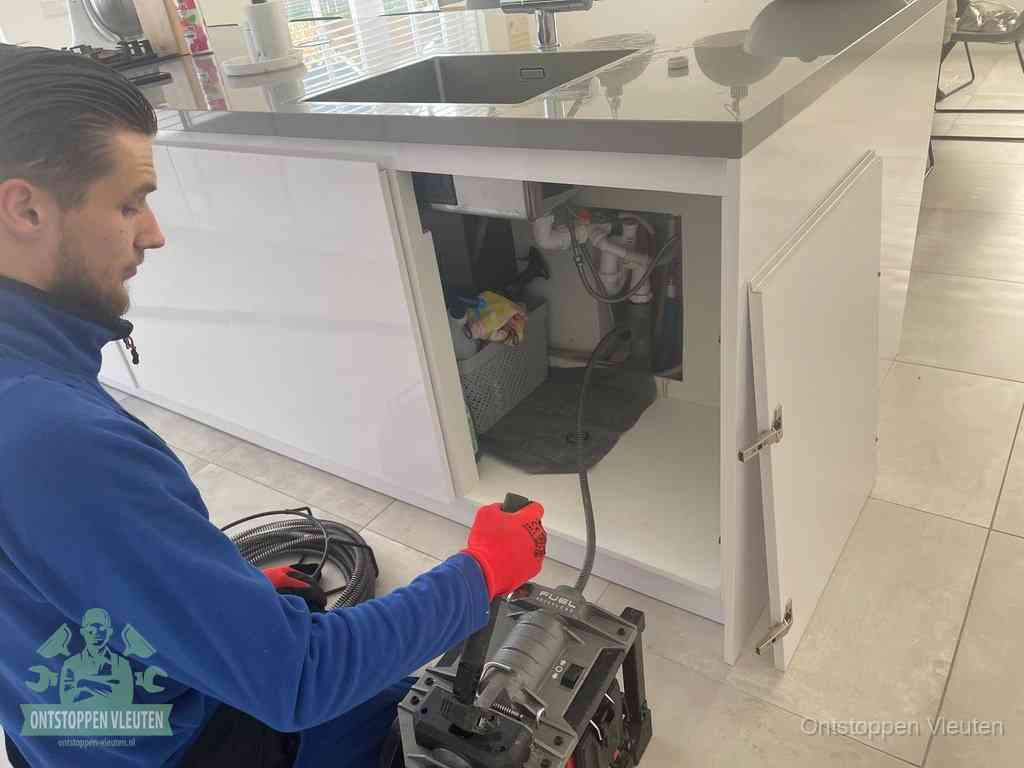 Monteur ontstopt met een veermachine een verstopte afvoer onder de gootsteen in Vleuten