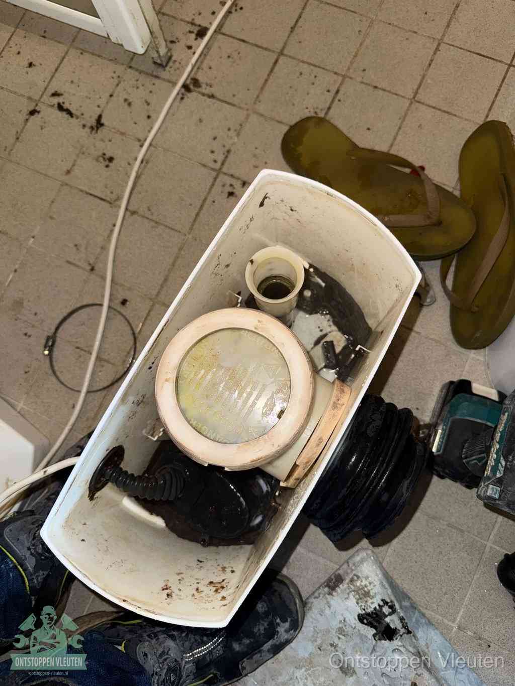 Een gedemonteerde toiletpot op de vloer met ontstoppingsveer en gereedschap ernaast, het verwijderen van een vastzittend voorwerp uit de wc in Vleuten