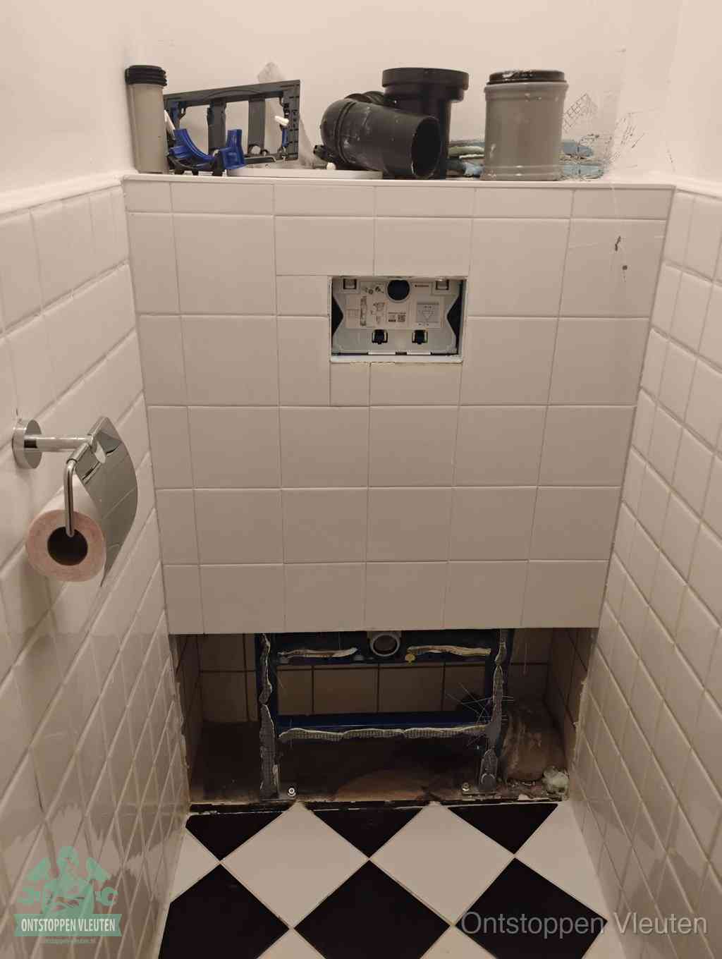 Een toiletruimte waar het hangtoilet en de inbouwreservoir-onderdelen zijn vrijgelegd voor onderhoud, periodiek nazicht voorkomt een wc-verstopping in Vleuten