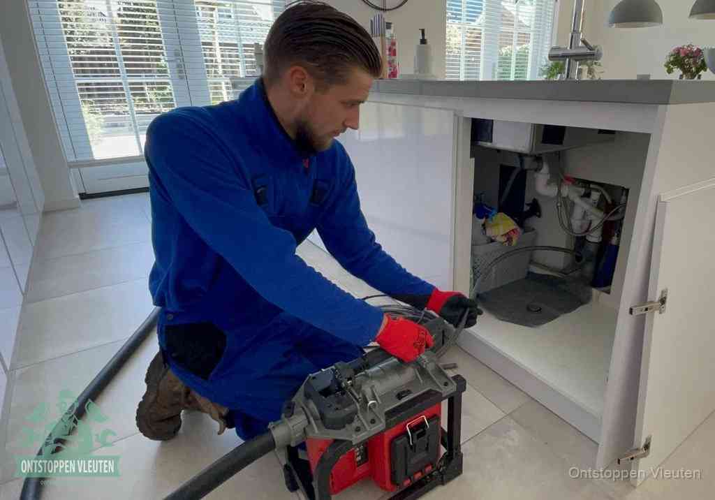 Een monteur voert een professionele elektrische ontstoppingsmachine in de afvoer onder de spoelbak tijdens het gootsteen ontstoppen in Vleuten